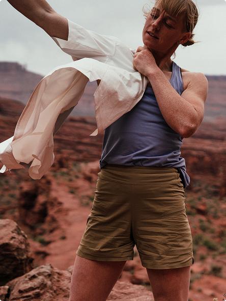 Woman putting on a white shirt over a tank top in a red rock desert.