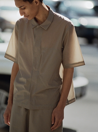 A person wearing a beige short-sleeved shirt with sheer banded sleeves and matching shorts, looking down.