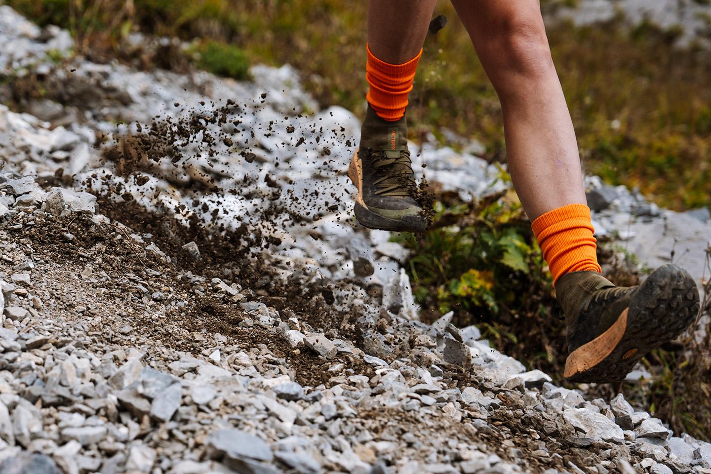a person wearing orange socks and trail running shoes is running on a rocky trail