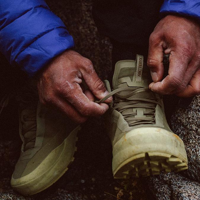 Person's hands tying the laces of a tan Arc'teryx hiking boot.