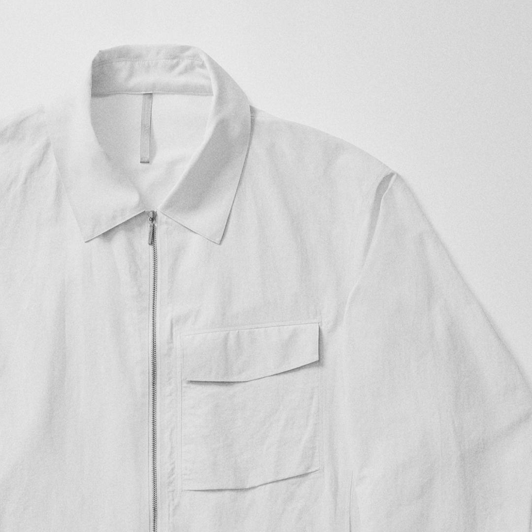 White collared zip-up shirt with a flap chest pocket.