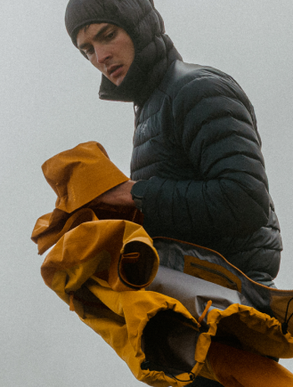 a man wearing a yellow jacket and blue pants is walking on a mossy hillside .