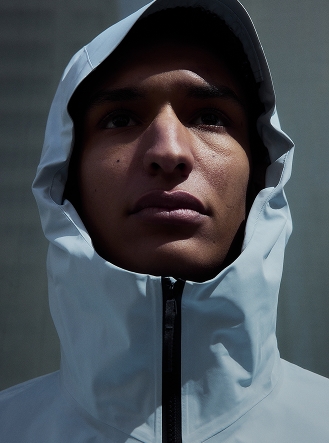 Close-up of a person in a light grey hooded jacket, looking up, with dramatic lighting on their face.