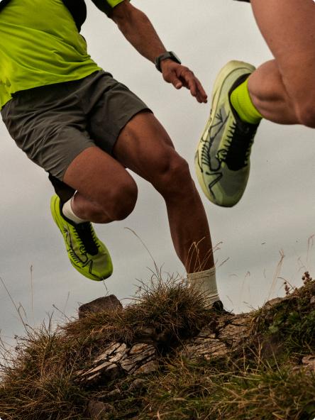 A trail runner in bright green shoes and shirt jumps over rocky terrain.