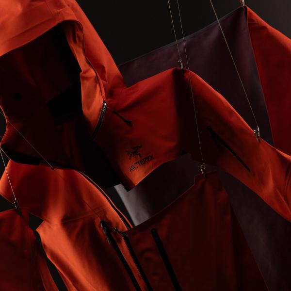 Multiple orange Arc'teryx jackets hanging in a dark space.