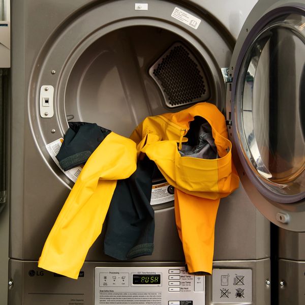 An open commercial dryer with yellow and dark clothes spilling out, stacked on top of a commercial washer.
