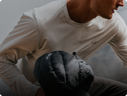 A person wearing a light long-sleeved Arc'teryx shirt holds a black puffy Arc'teryx item.