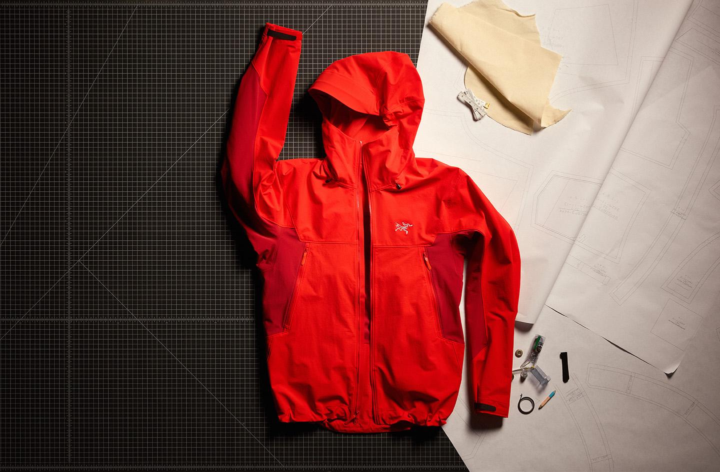 a red softshell climbing jacket with a hood is sitting on top of a cutting board