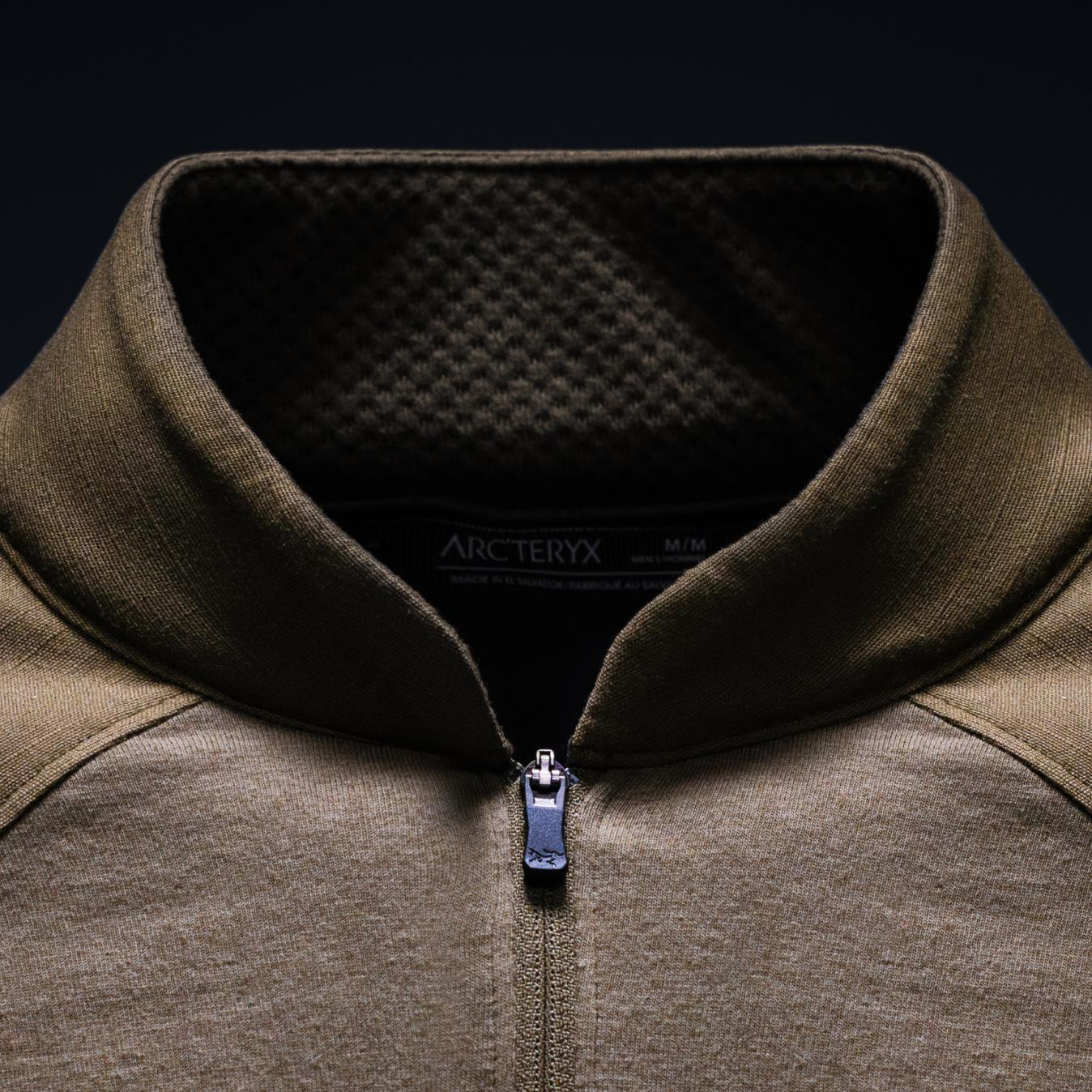 Close-up of an olive green Arc'teryx quarter-zip top, showing the brand tag, ribbed collar, and metallic zipper.