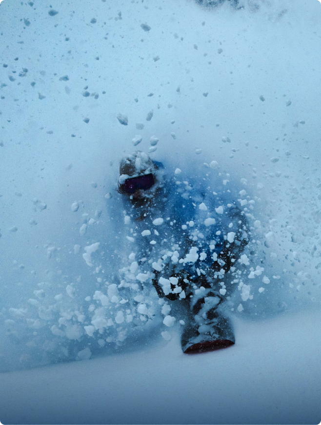 Snowboarder carving a turn, engulfed in a dramatic spray of powder.