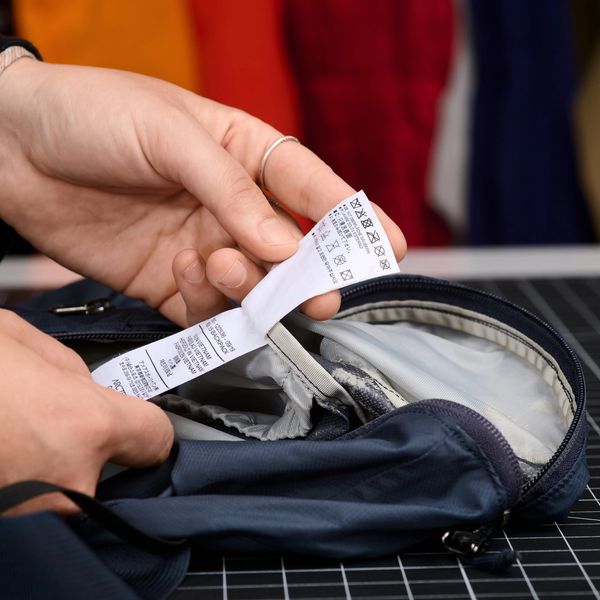 Person's hands examining a white clothing label inside a dark blue bag.