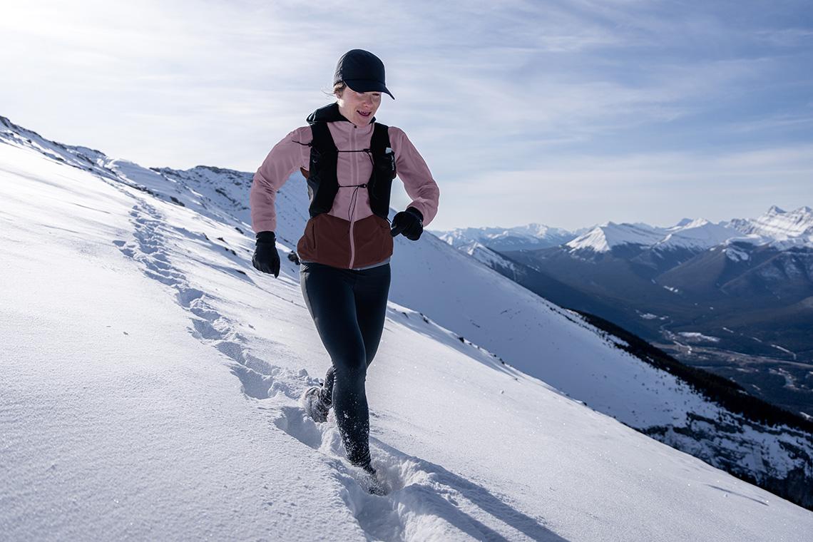 a woman is running on top of a snow covered mountain in mountain running gear