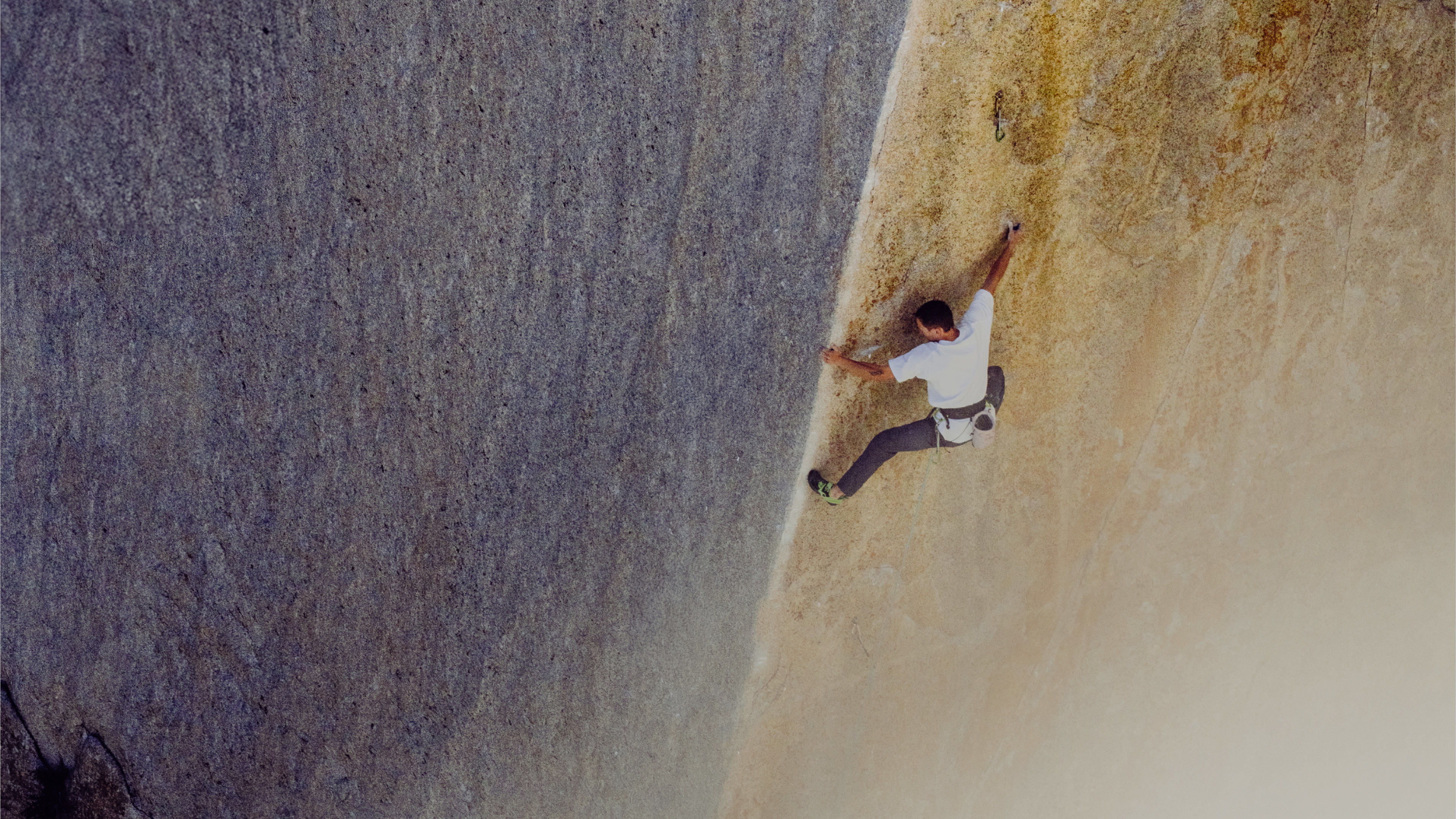 A man in a white shirt and dark pants rock climbs on a massive, two-toned rock face.