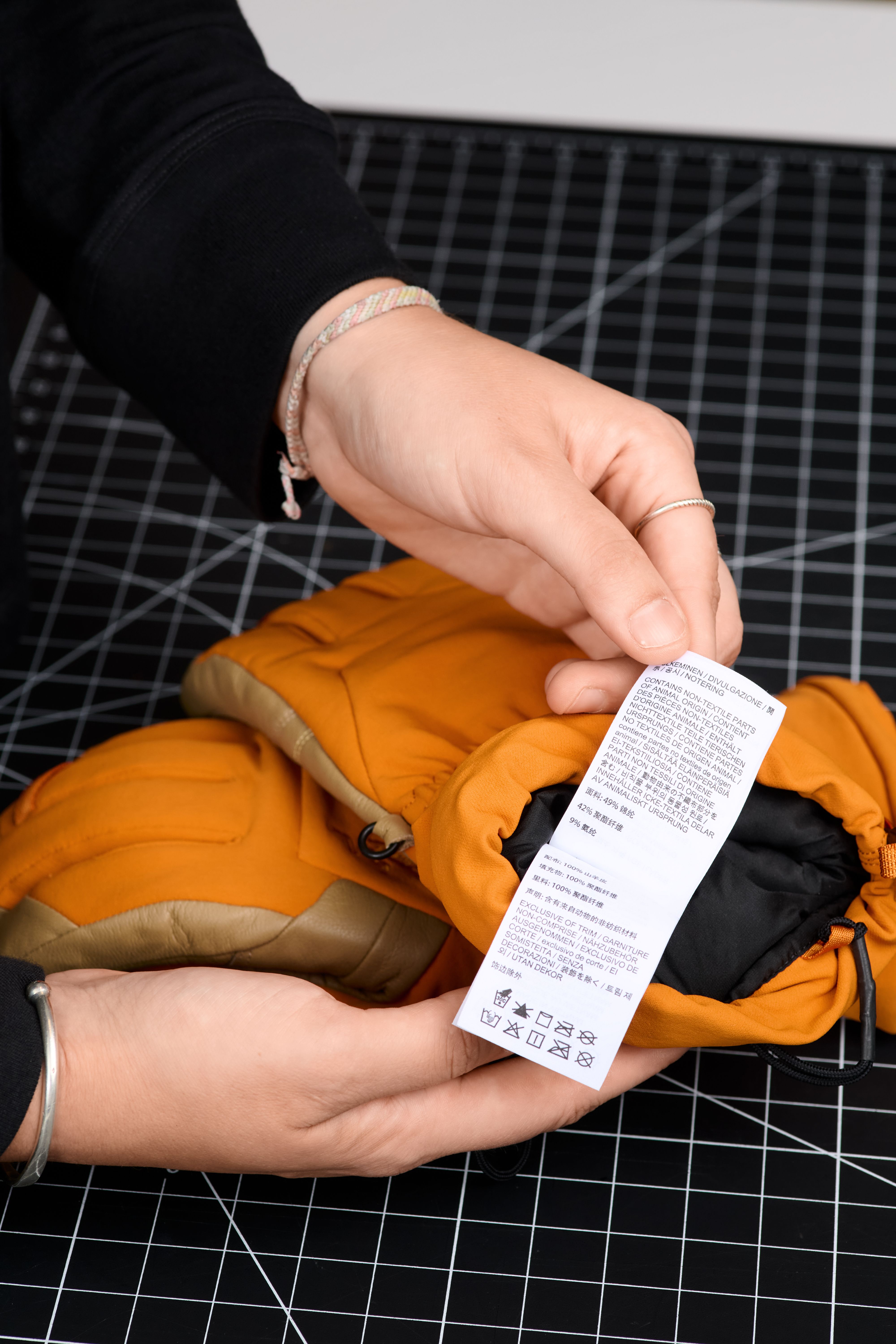 Close-up of hands holding an orange glove and examining its white care label.