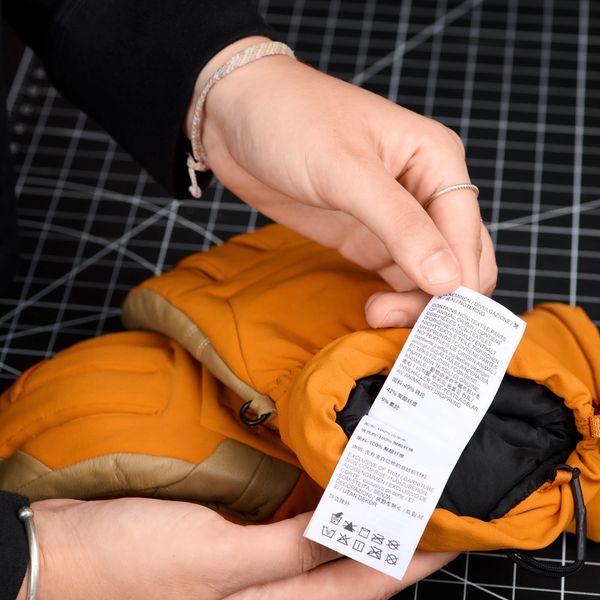 Close-up of hands holding an orange glove and examining its white care label.