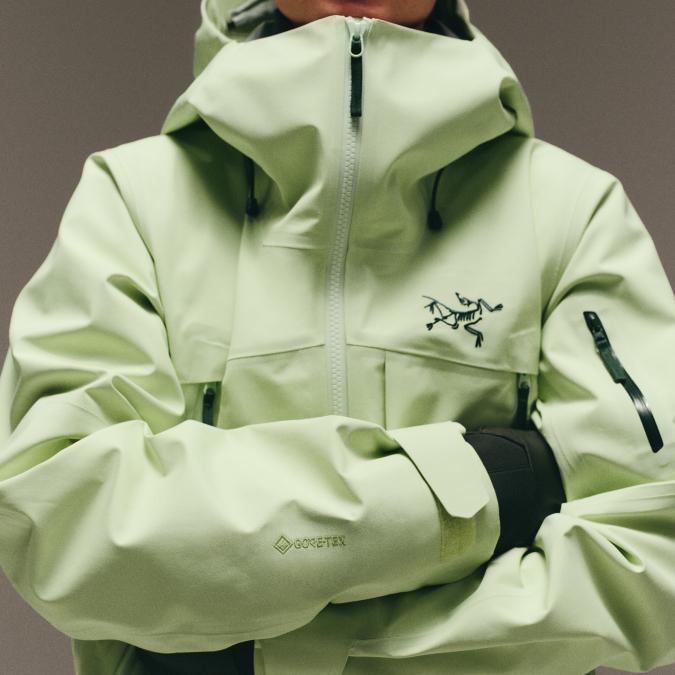 A person wears a lime green Arc'teryx Gore-Tex jacket with arms crossed.