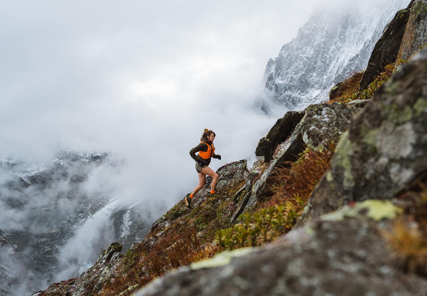 a woman in trail running shoes is running down a rocky hillside in the mountains
