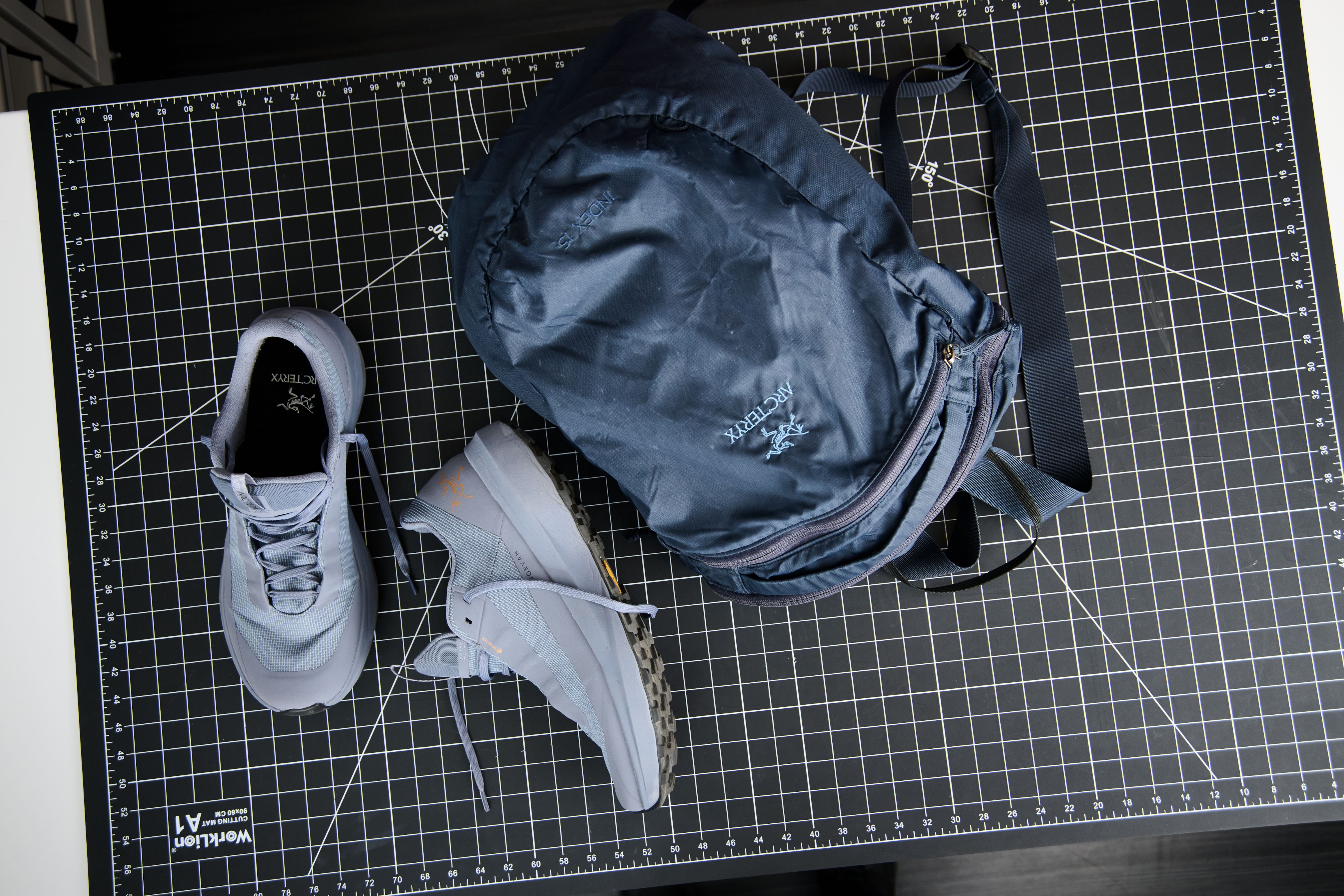 Arc'teryx running shoes and a backpack on a grid mat.