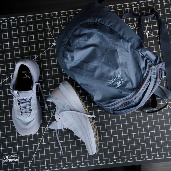 Arc'teryx running shoes and a backpack on a grid mat.
