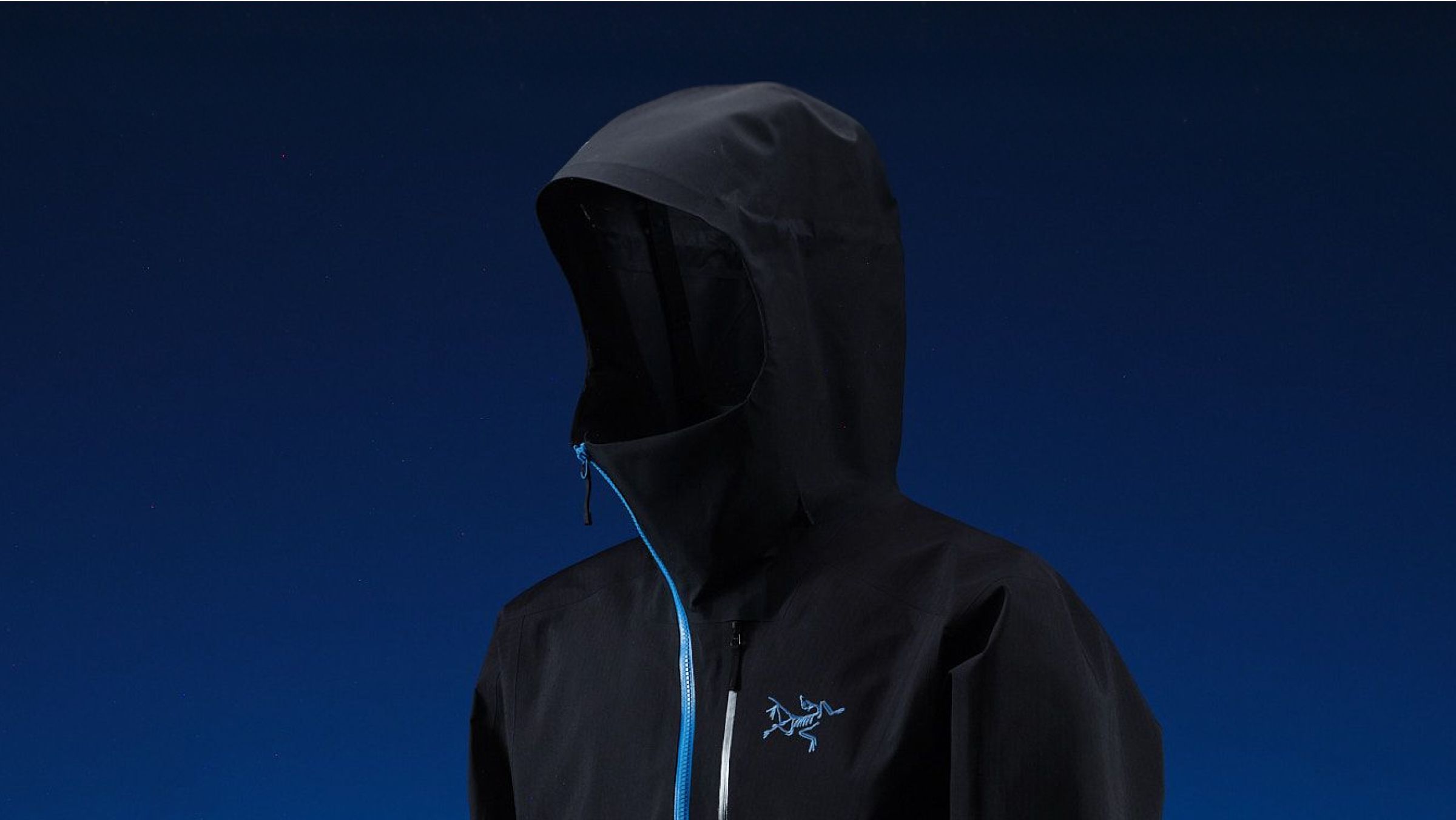 Black Arc'teryx jacket with hood up, blue zipper, and blue logo on a dark blue background.
