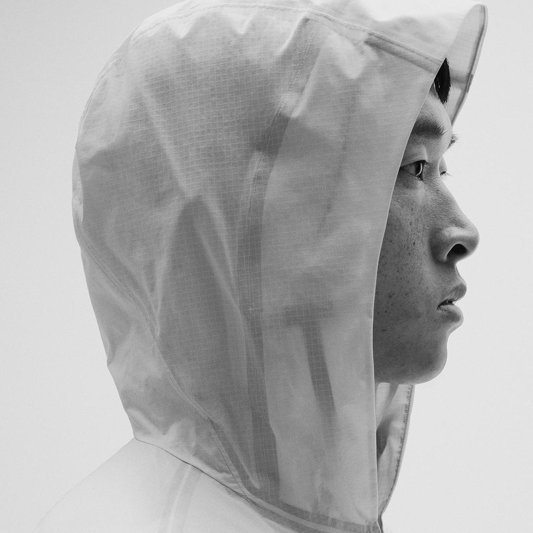 Black and white profile of a man wearing a translucent ripstop hooded jacket.