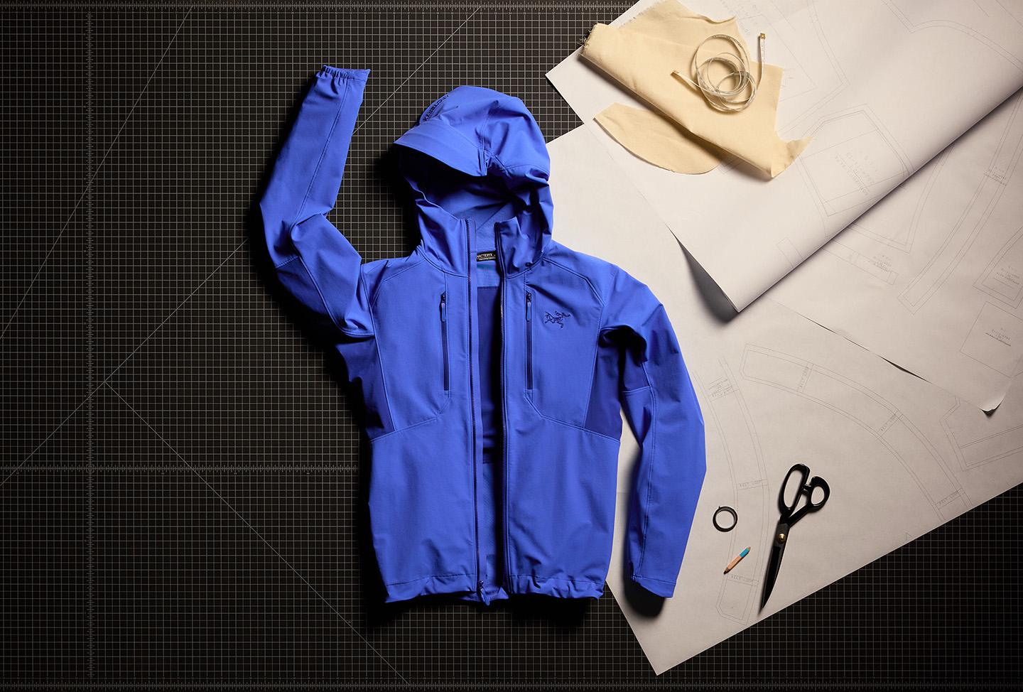 a blue softshell jacket is sitting on top of a cutting board next to scissors and a piece of paper
