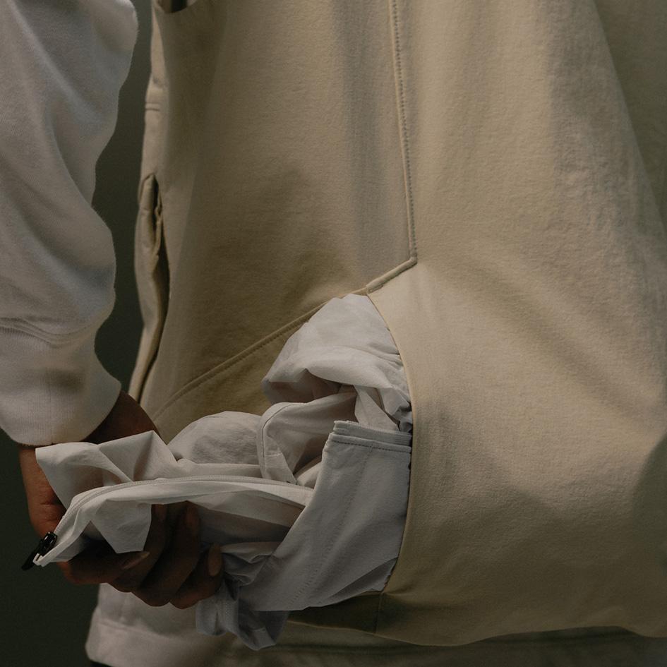 A person wearing a cream vest, using a large side pocket to hold crumpled white fabric.