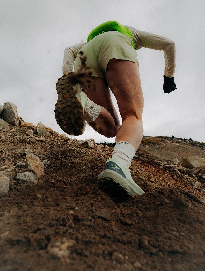 A trail runner climbs a steep, rocky dirt path, kicking up soil with their lead foot.