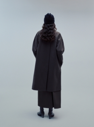 Rear view of a person wearing a dark beanie, long dark coat, and dark boots.