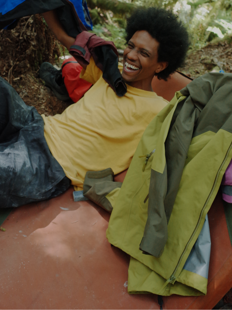 A person with an afro laughs happily while reclining outdoors, holding up clothing.