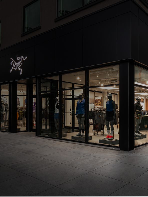 An Arc'teryx store at night, with its illuminated logo and a display of outdoor gear in the windows.