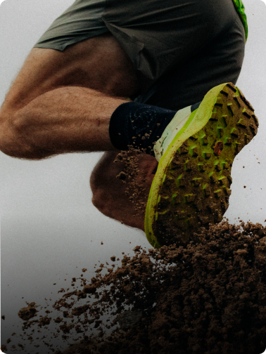 Foot in a green trail running shoe kicking up dirt.
