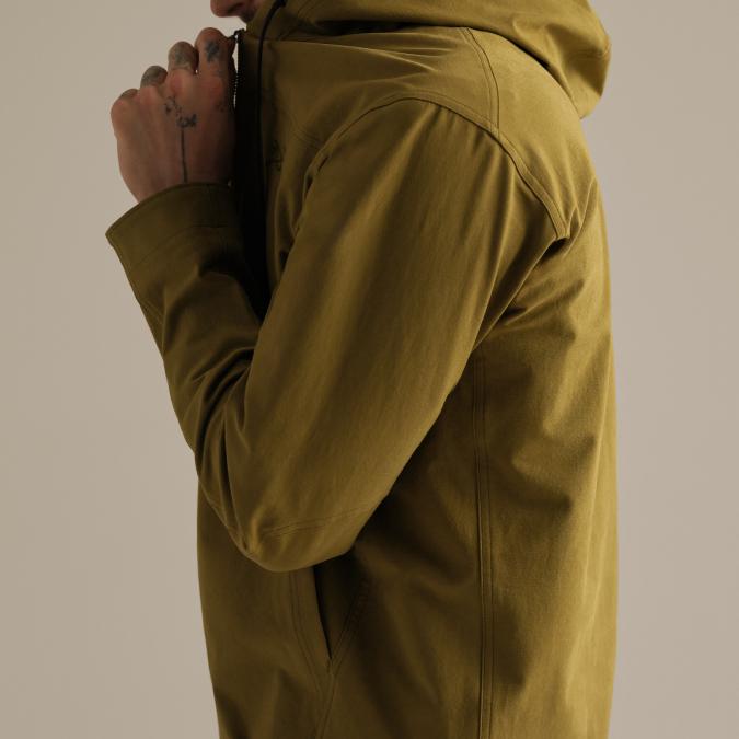 Person in a dark olive green hooded jacket with a tattooed hand near their chin.