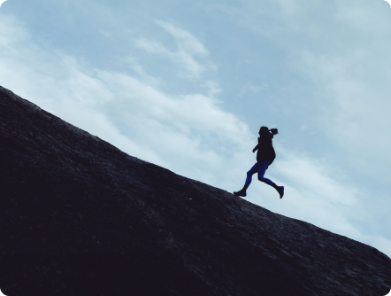 Silhouette of a person running up a steep rock face against a cloudy sky.