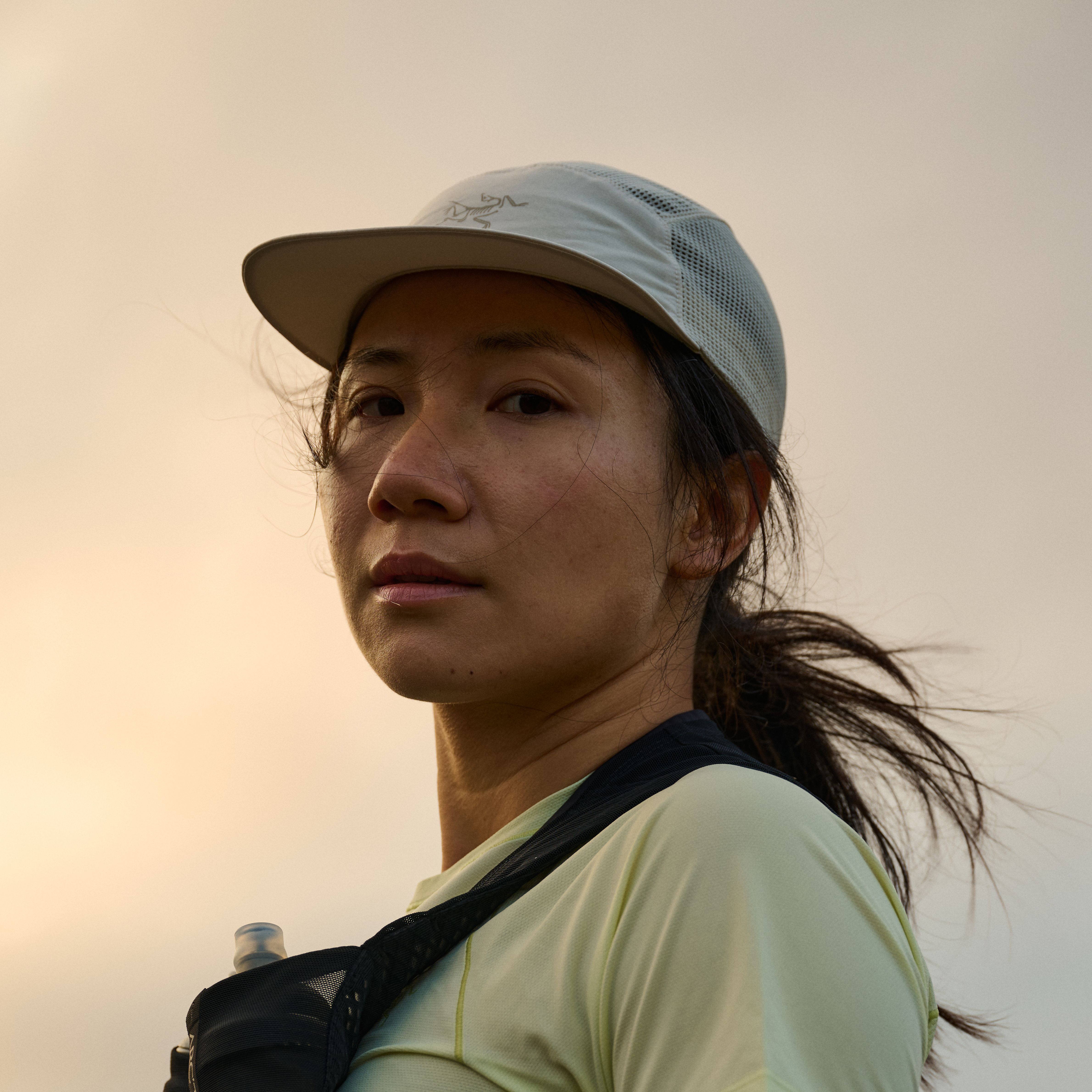Fuzhao Xiang in a light athletic cap and running vest looks forward, her hair windswept, against a soft sky.