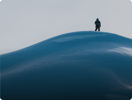 A person stands atop a snow dune against a pale sky.
