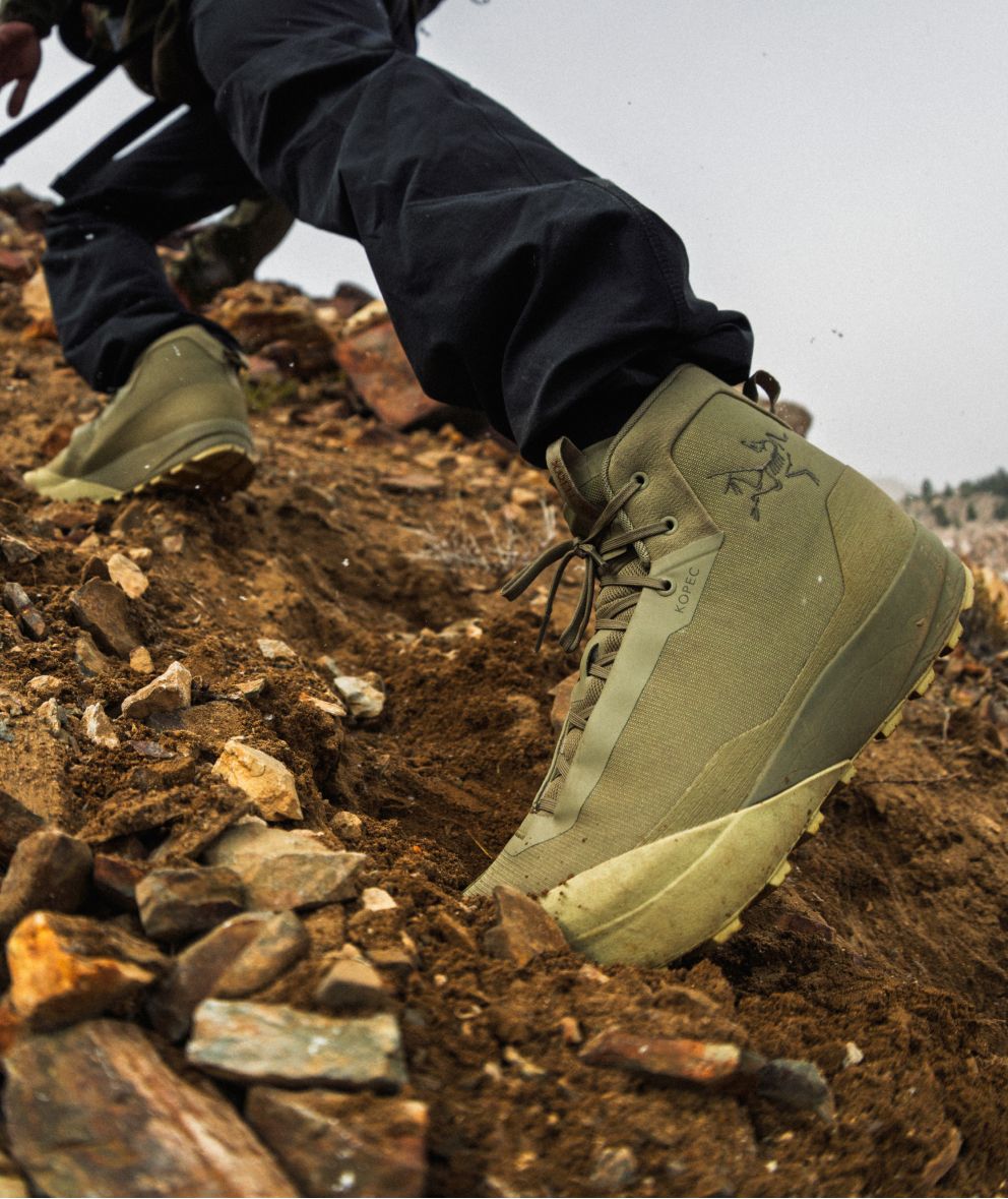 A person's feet in Arc'teryx Kopec olive green hiking boots stepping on a steep, rocky dirt path.
