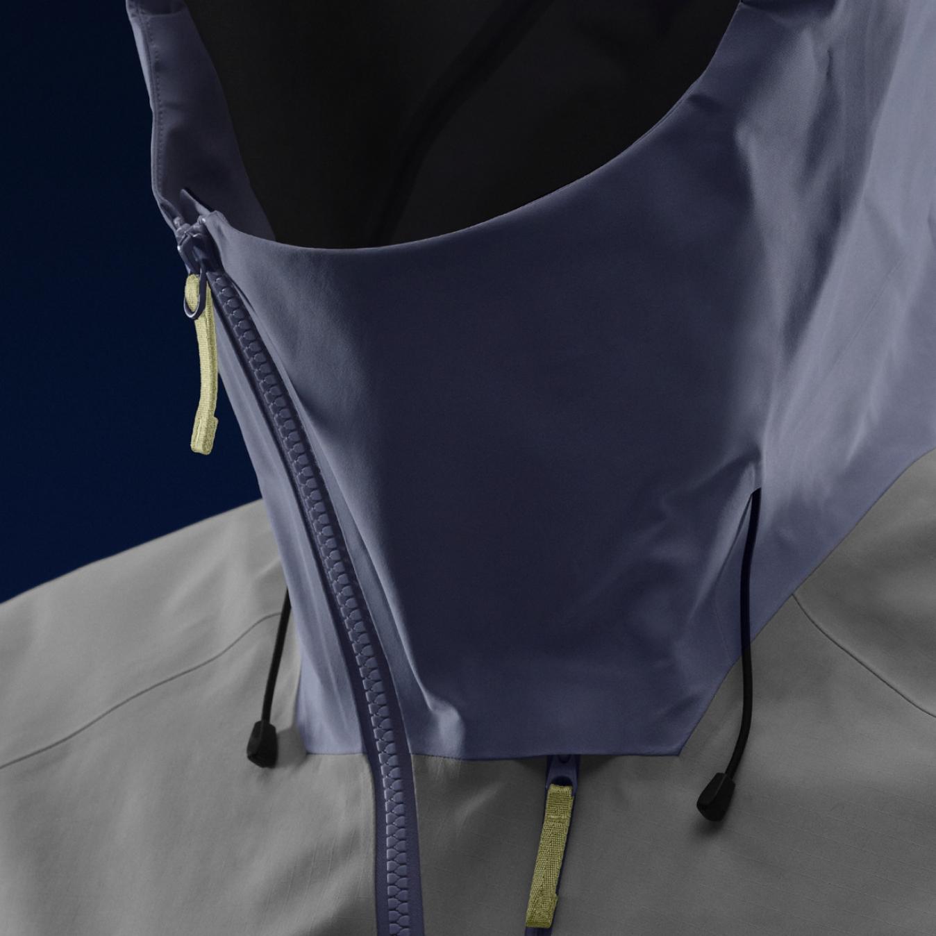 Close-up of a two-tone jacket with a light grey body and purple hooded collar, featuring zippers with yellow pulls and black drawstrings.
