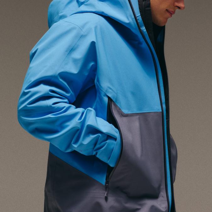 A person wearing a blue and grey hooded jacket with a hand in the pocket.
