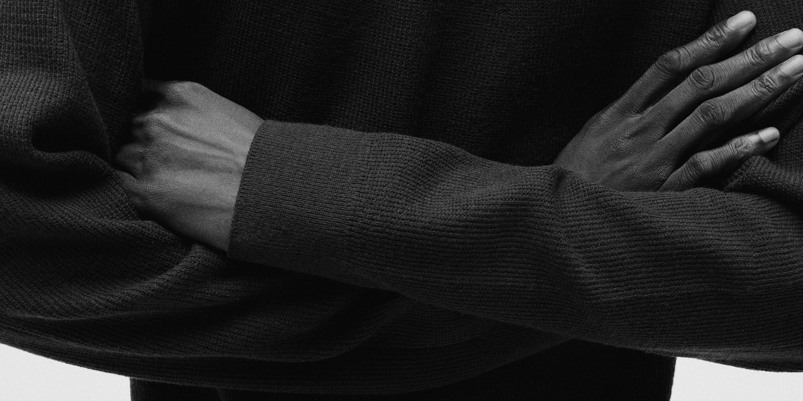 a black and white photo of a person wearing a black sweater with their arms crossed .