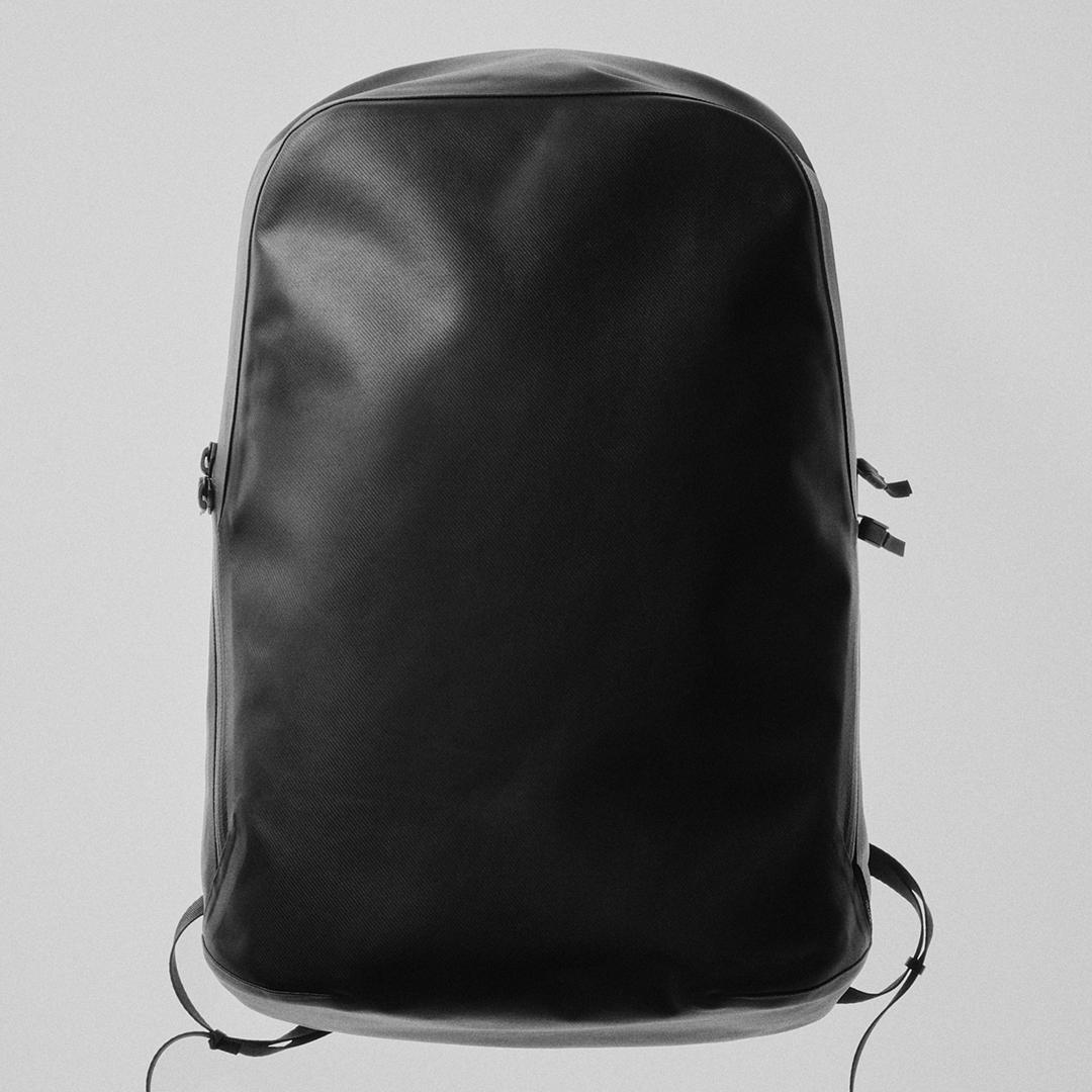 A black, minimalist backpack with a rounded top and side zippers.