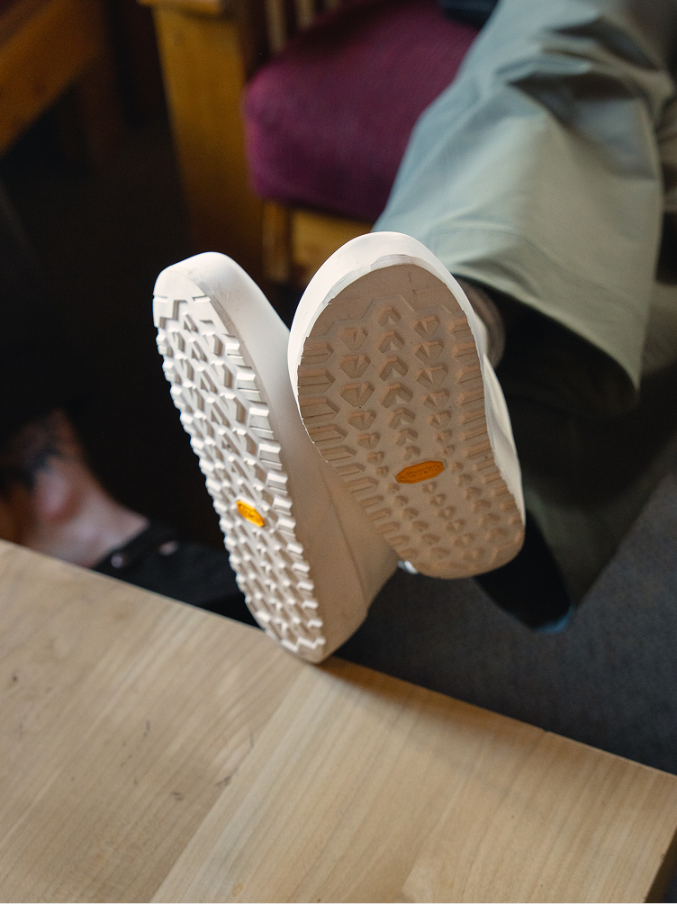 Soles of light-colored shoes with textured Vibram treads resting on a wooden surface.