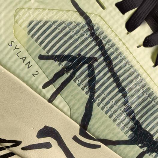 Close-up of a light green shoe detail showing "SYLAN 2" text, black laces, a striped translucent overlay, and irregular black markings.