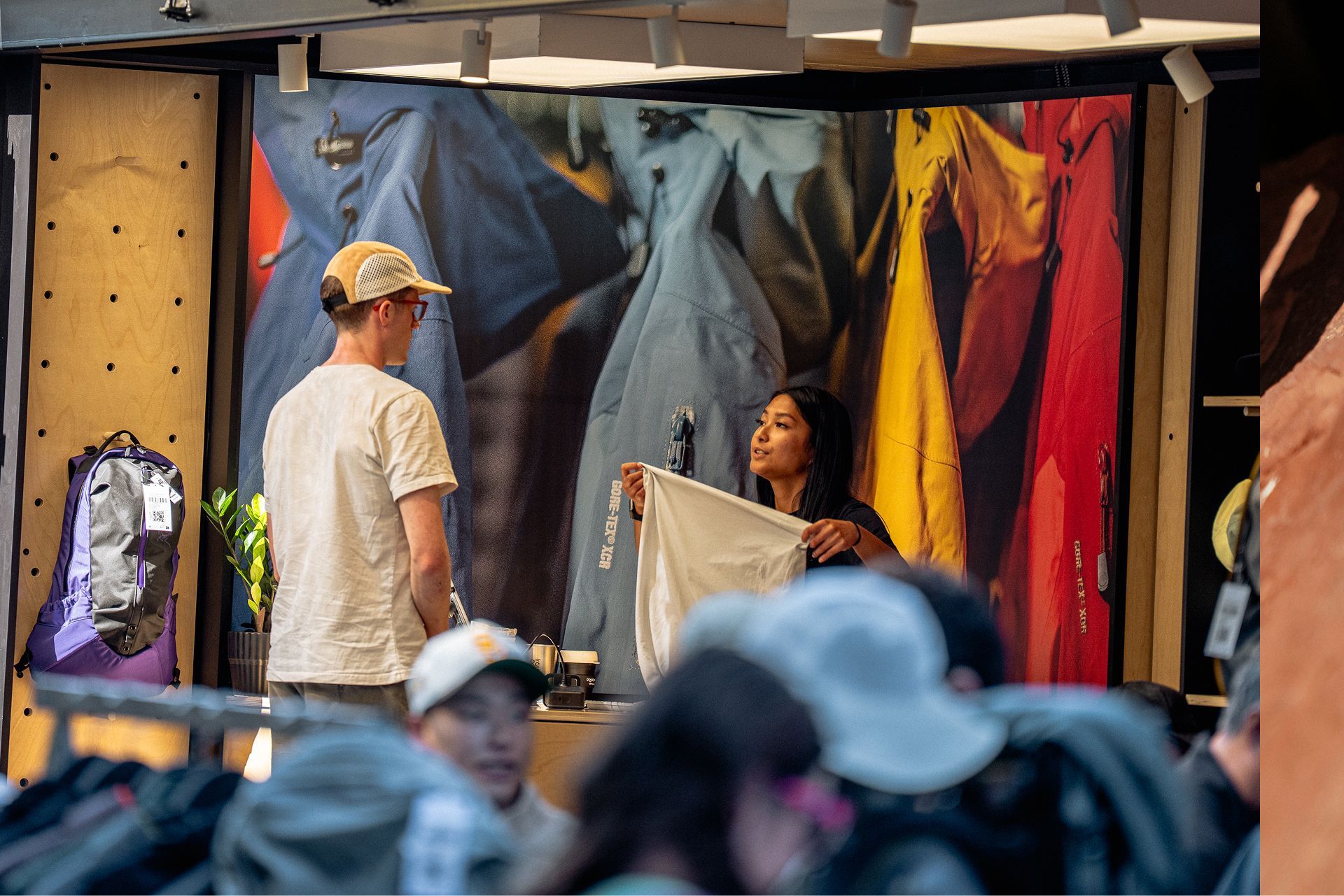 A woman holds up a white shirt for a man in an outdoor clothing store.