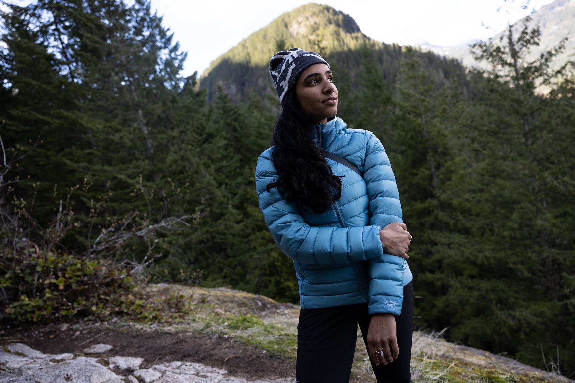 Woman in a blue puffer jacket and beanie looking out over a forest with mountains.