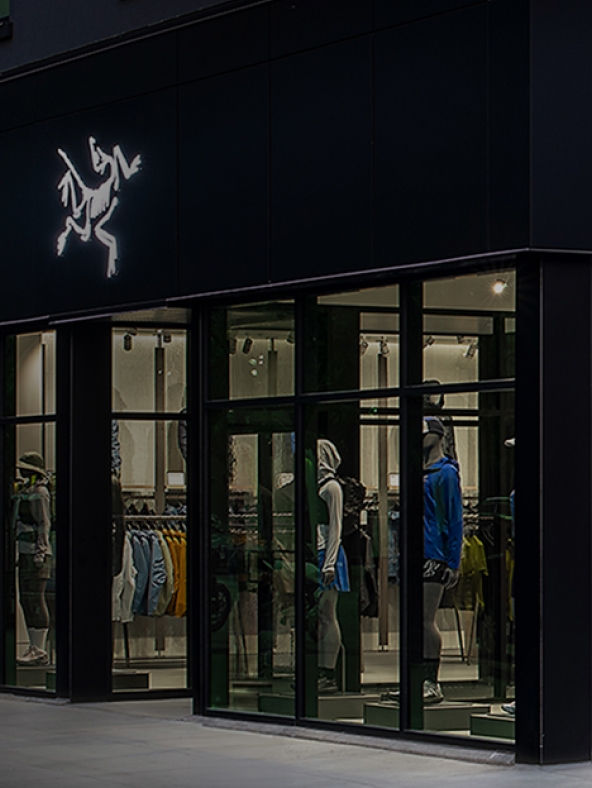 Arc'teryx store at night with its glowing logo and mannequins in the display windows.