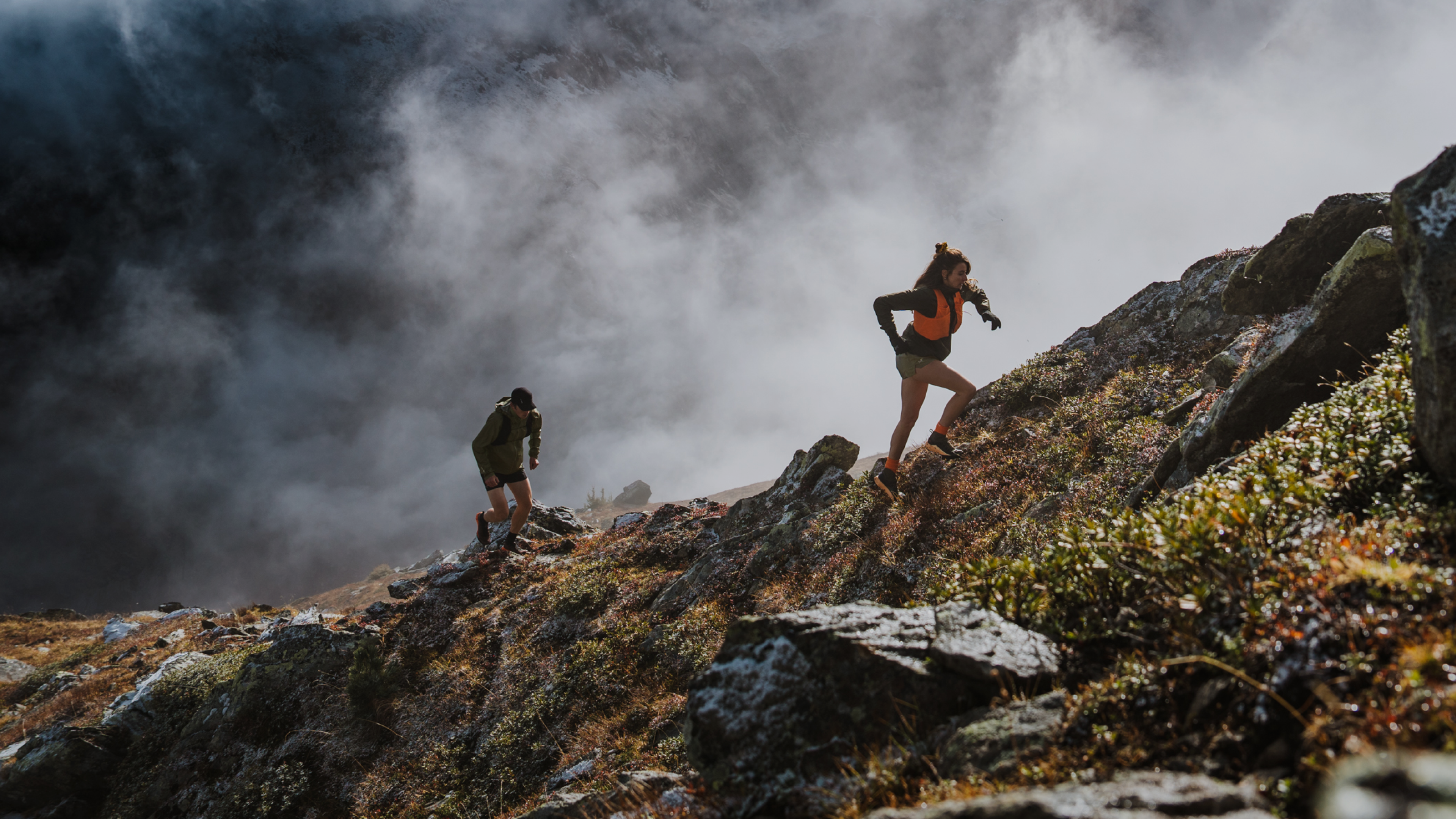Two people trail running up a foggy, rocky mountain.