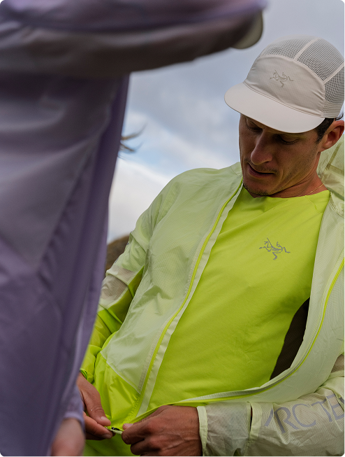 A man in a lime green Arc'teryx jacket and white mesh cap zips his jacket.