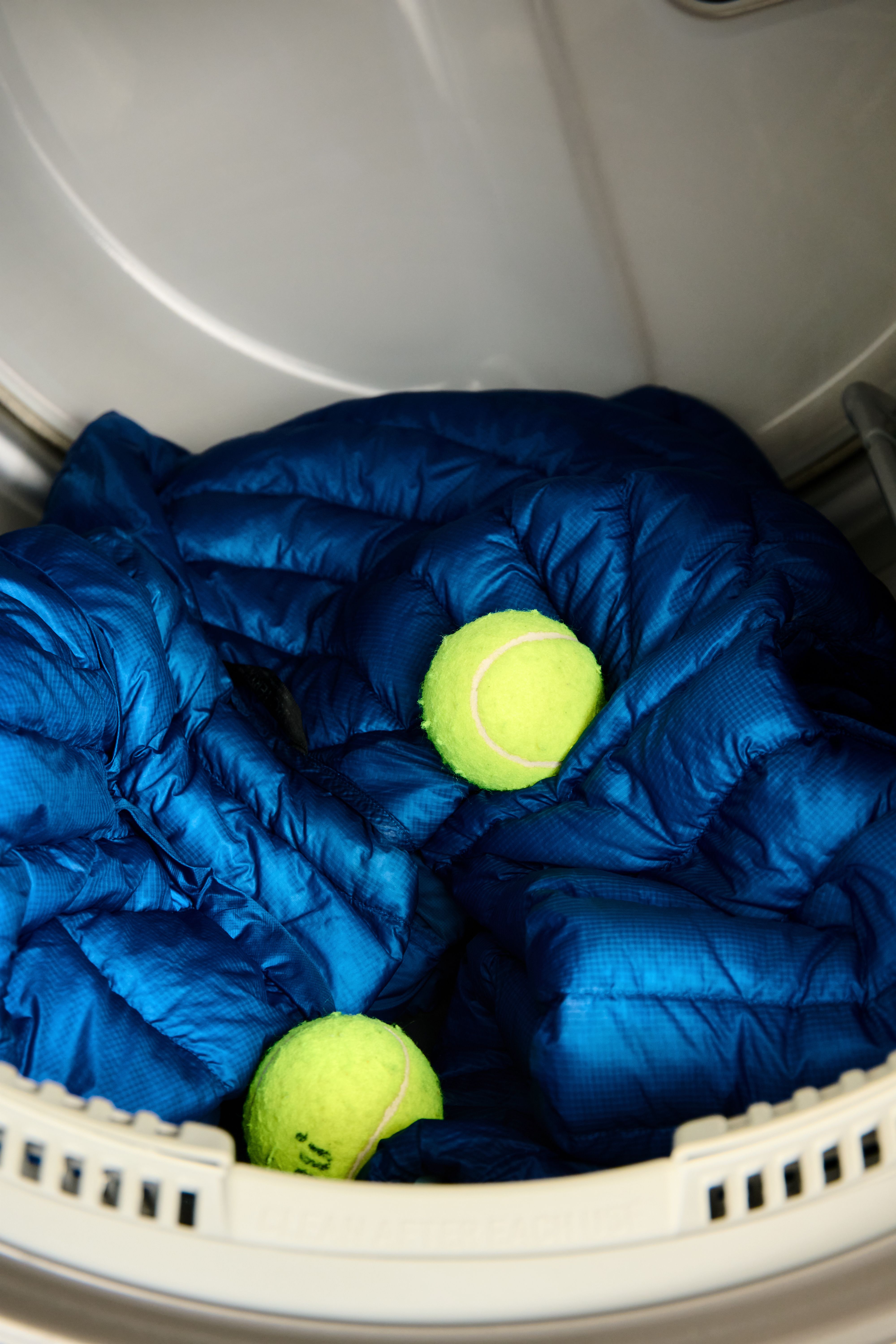 Blue down jacket and two tennis balls in a dryer.