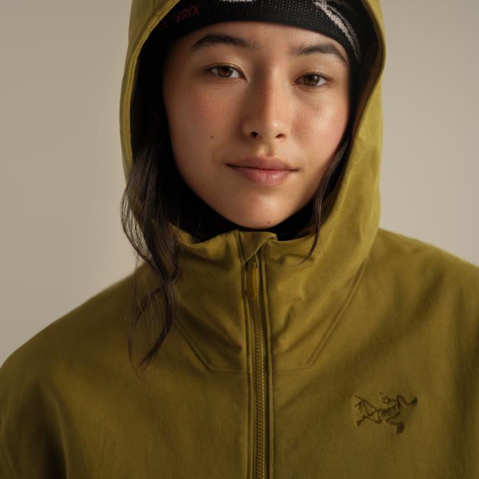 Close-up of a woman wearing an olive green Arc'teryx hooded jacket and black headband.